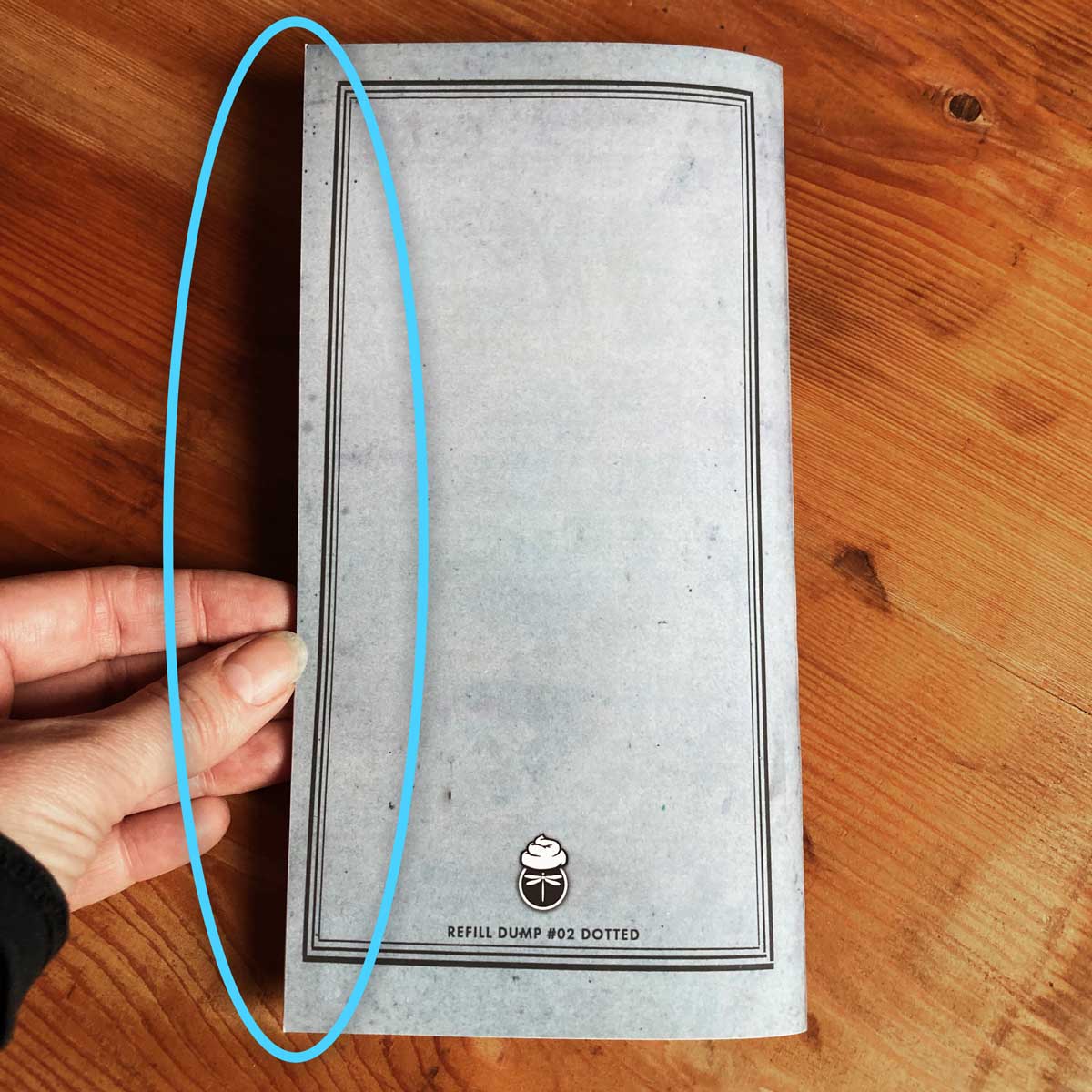 Image shows a hand holding this "Big Dump Journal" in front of a wooden surface. The slightly off trim-angle is highlighted for the viewer.