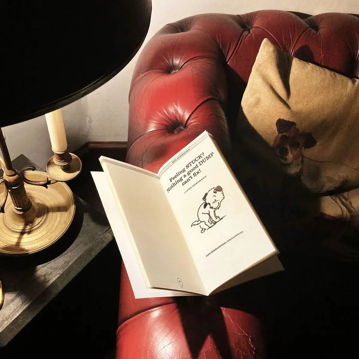 An open version of a Little Hunterman's Dump-Journal on an armrest showing an dotted page and the doggie dump-quote "Feeling stuck? Nothing a good cump can't fix!"