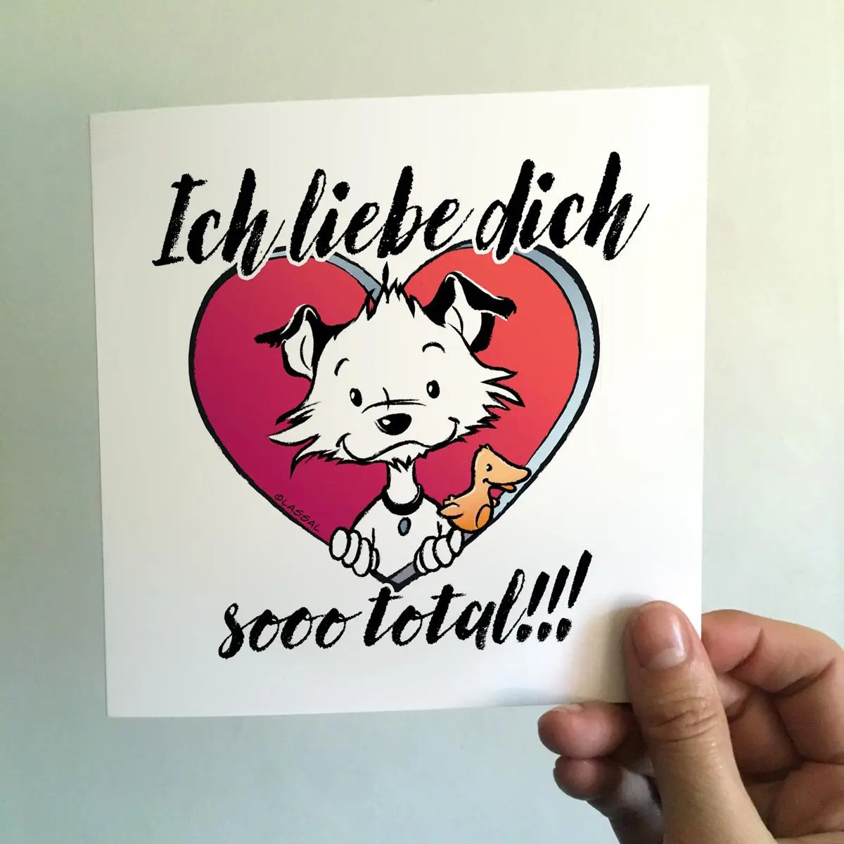 Front of square Little Hunterman card showing him and Flynn looking out of a big red heart with large text saying in German: Ich liebe dich sooo total!!! With a hand holding the card agains a light background