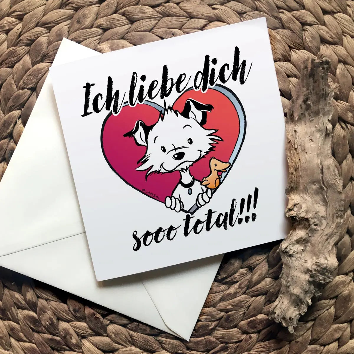 Front of square Little Hunterman card showing him and Flynn looking out of a big red heart with large text saying in German: Ich liebe dich sooo total!!! With closed card and envelope on a natural surface with one of Hunter's wooden sticks.