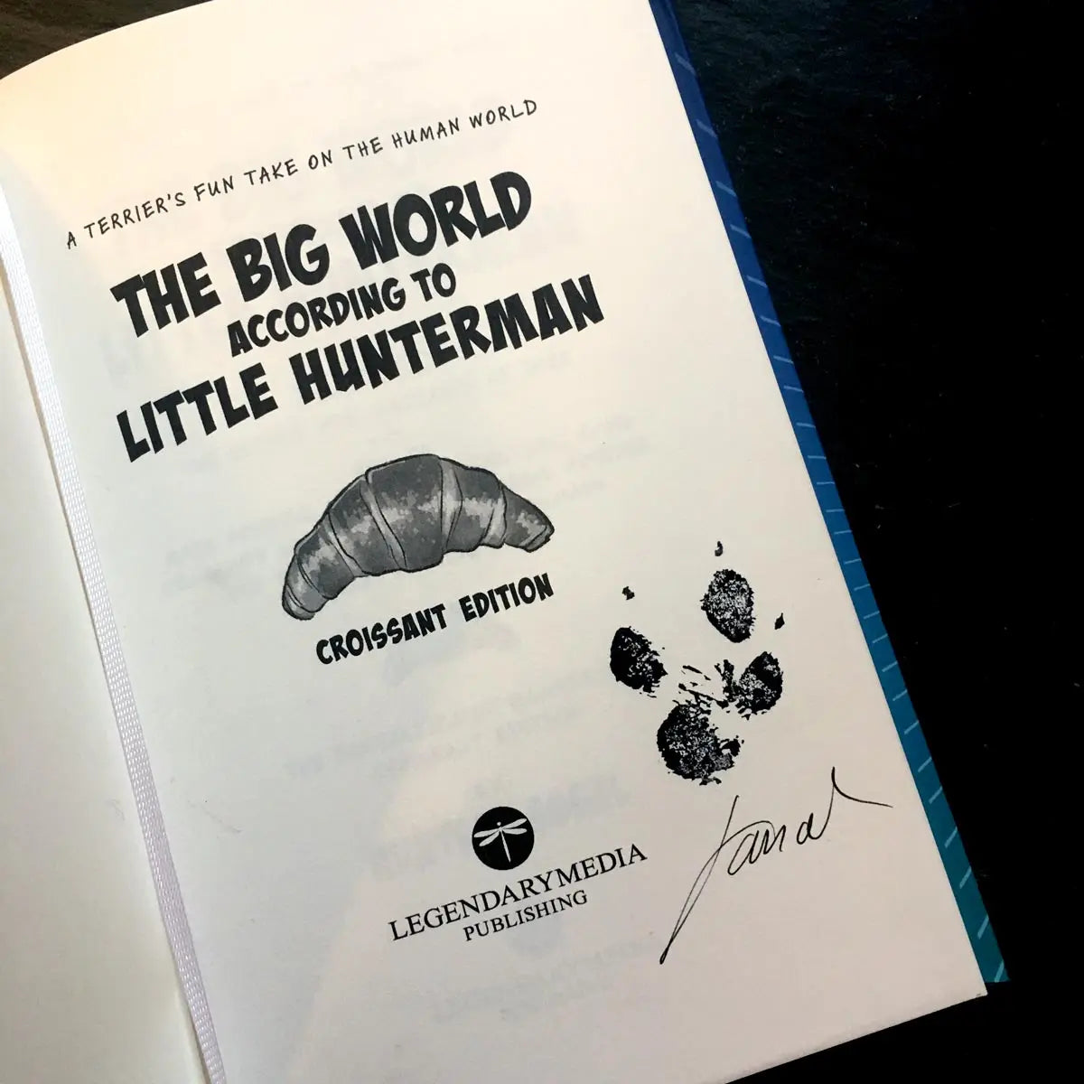 The Big World According to Little Hunterman, retailer version hardcover with black and white illustrations and creme colored paper. The image shows the signed (by the human) and paw-grammed (by the dog) title page.