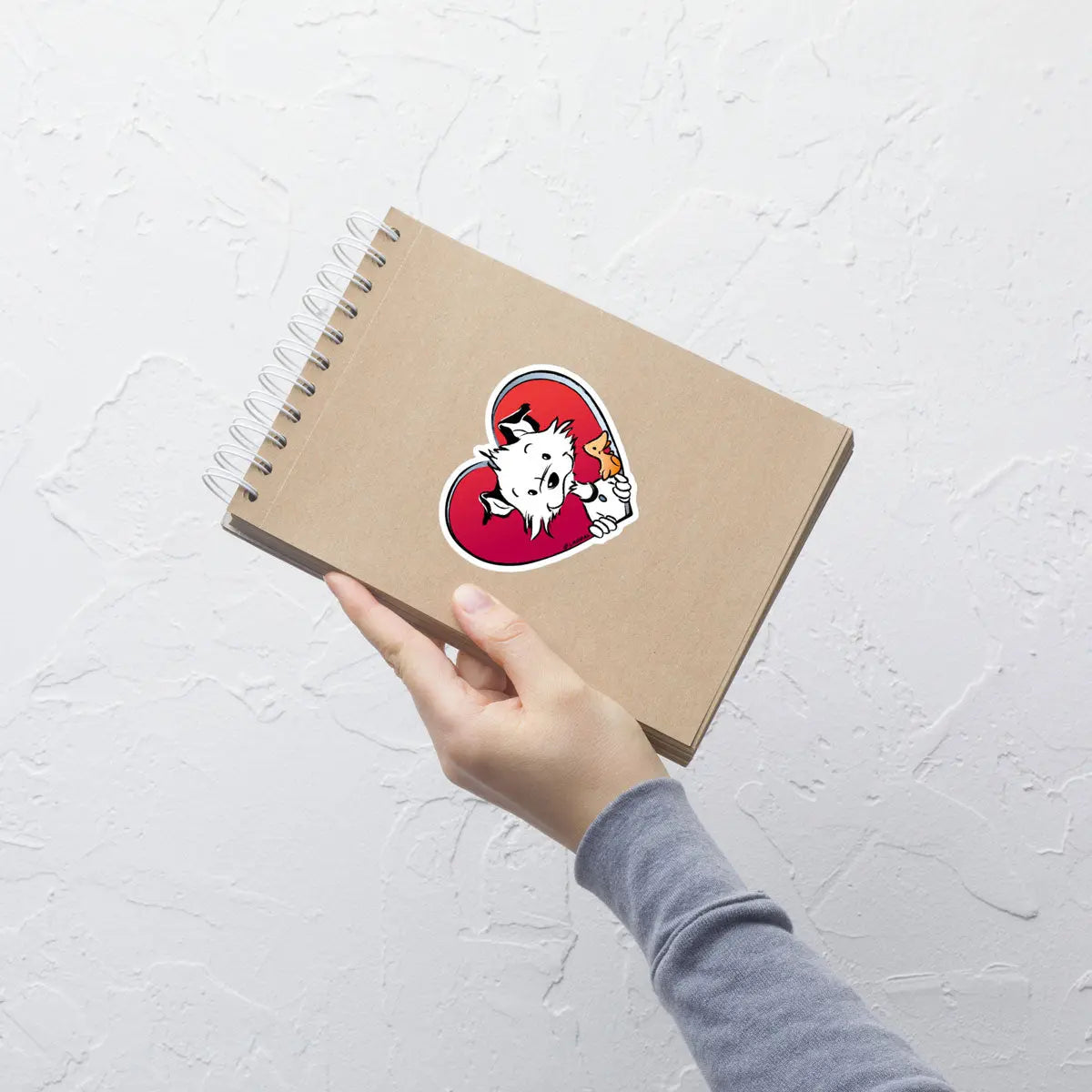 Image shows a hand holding a notepad with one of Little Hunterman's "Sticky Doggie Love" stickers glued to the front.