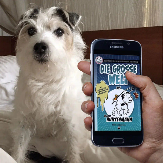 A photo of Little Hunterman with a hand holding a smartphone showing the cover of Hunter Lassal's eBook "Die große Welt des kleinen Huntermann"