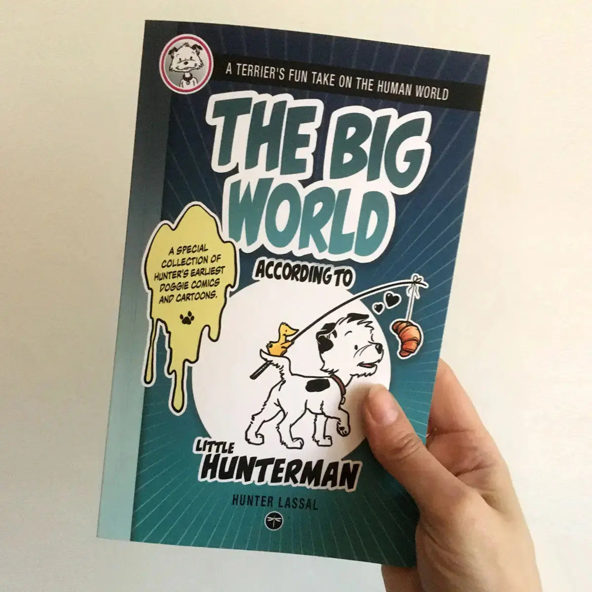The Big World According to Little Hunterman, retailer version paperback with black and white illustrations and creme colored paper. This image shows a hand holding the book against a light background with the cover facing forward.