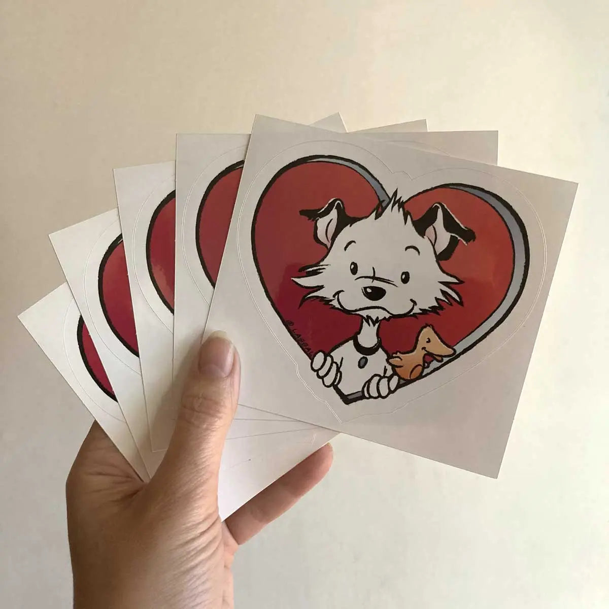 Image shows a hand holding a set of five of Little Hunterman's "Sticky Doggie Love" stickers in front of a light background.