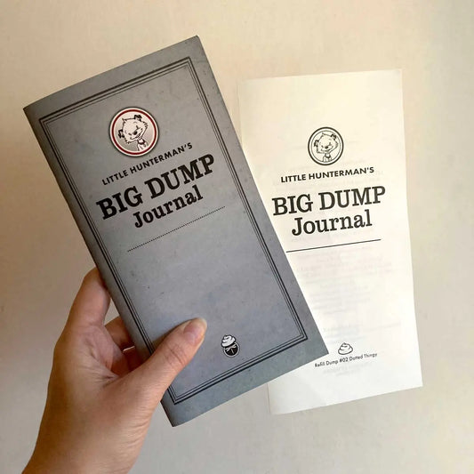 This image shows a hand holding a journal against a light background. The journal, one of Little Hunterman's BIG DUMP Journals, is seen with a separate spread that contains the title page (and the imprint on the back). These pages come included with the journal despite not being stapled to it. 