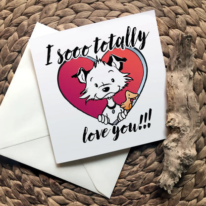 Image shows a square Little Hunterman card showing him and Flynn looking out of a big red heart with large text saying: I sooo totally love you!!! With closed card and envelope on a natural surface with one of Hunter's wooden sticks.