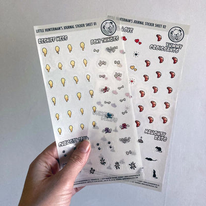 A hand holding one of Little Hunterman's Journal Sticker Sheets 01 and 02 up against a light background.