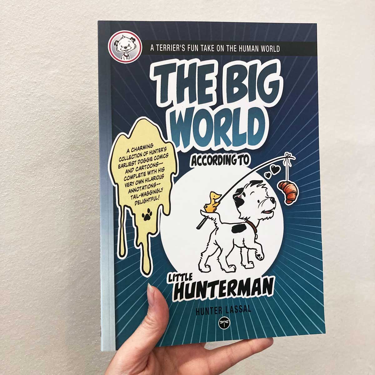 Hand holding a paperback version showing the front cover of the premium edition of The Big World According to Little Hunterman.