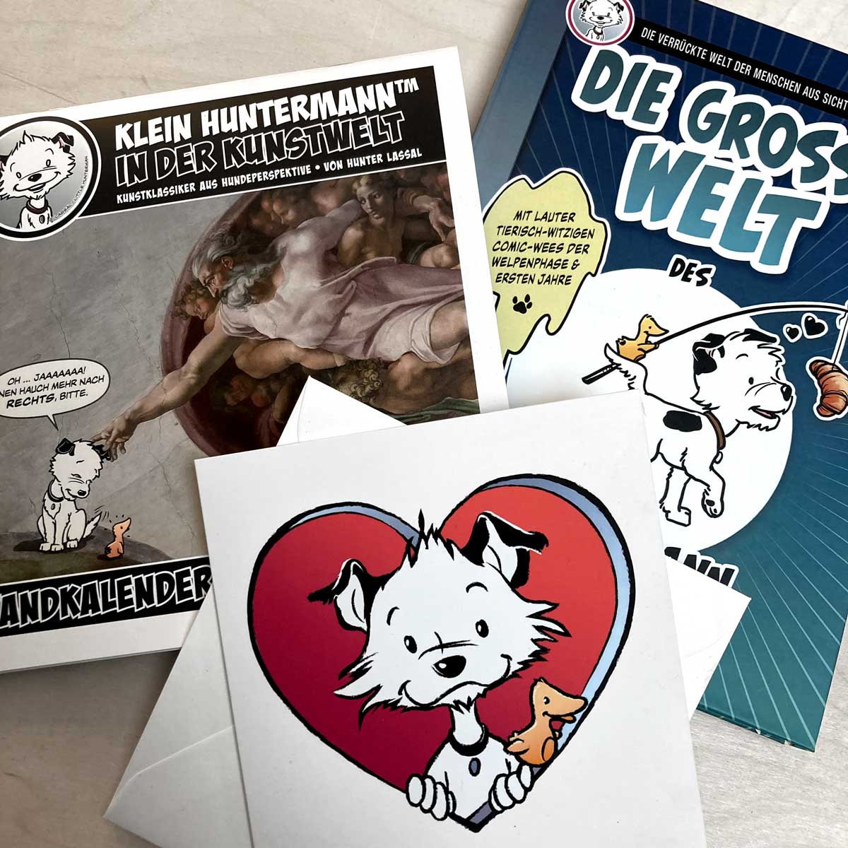 A German calendar, a German book, and a large card featuring a cartoon dog character on a light wooden surface