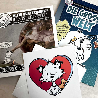 A German calendar, a German book, and a large card featuring a cartoon dog character on a light wooden surface