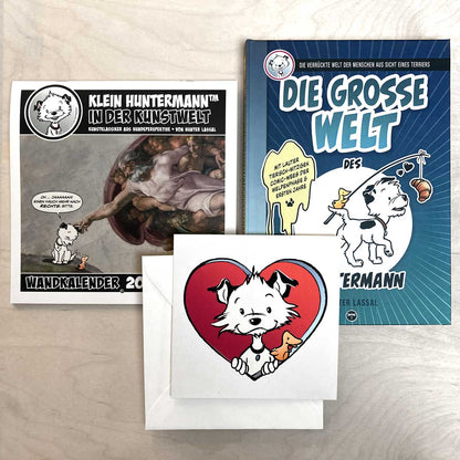 A German calendar, a German book, and a large card featuring a cartoon dog character on a light wooden surface